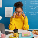 Curly haired student keeps both fingers on temples, tries to gather with thoughts, recalls information in mind